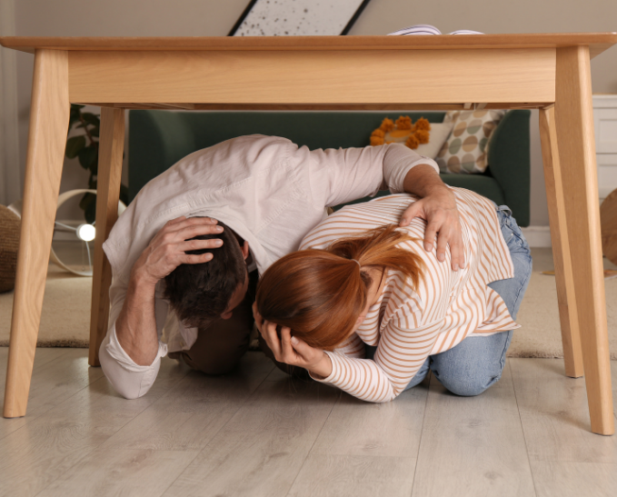 A couple taking cover under the table in their living room during an earthquake.